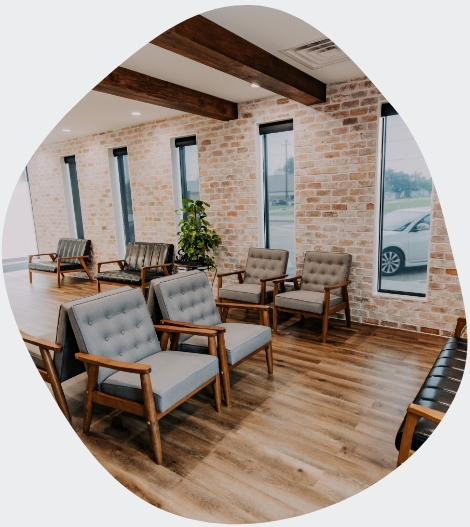 Modern dentist office waiting room in Pearland, Texas with stylish mid-century chairs, exposed brick walls, wood flooring, and tall windows creating a comfortable atmosphere for patients.